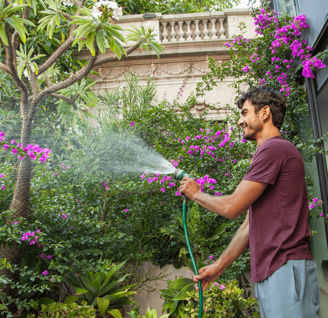 Foto de un hombre regando las plantas de su jardín.